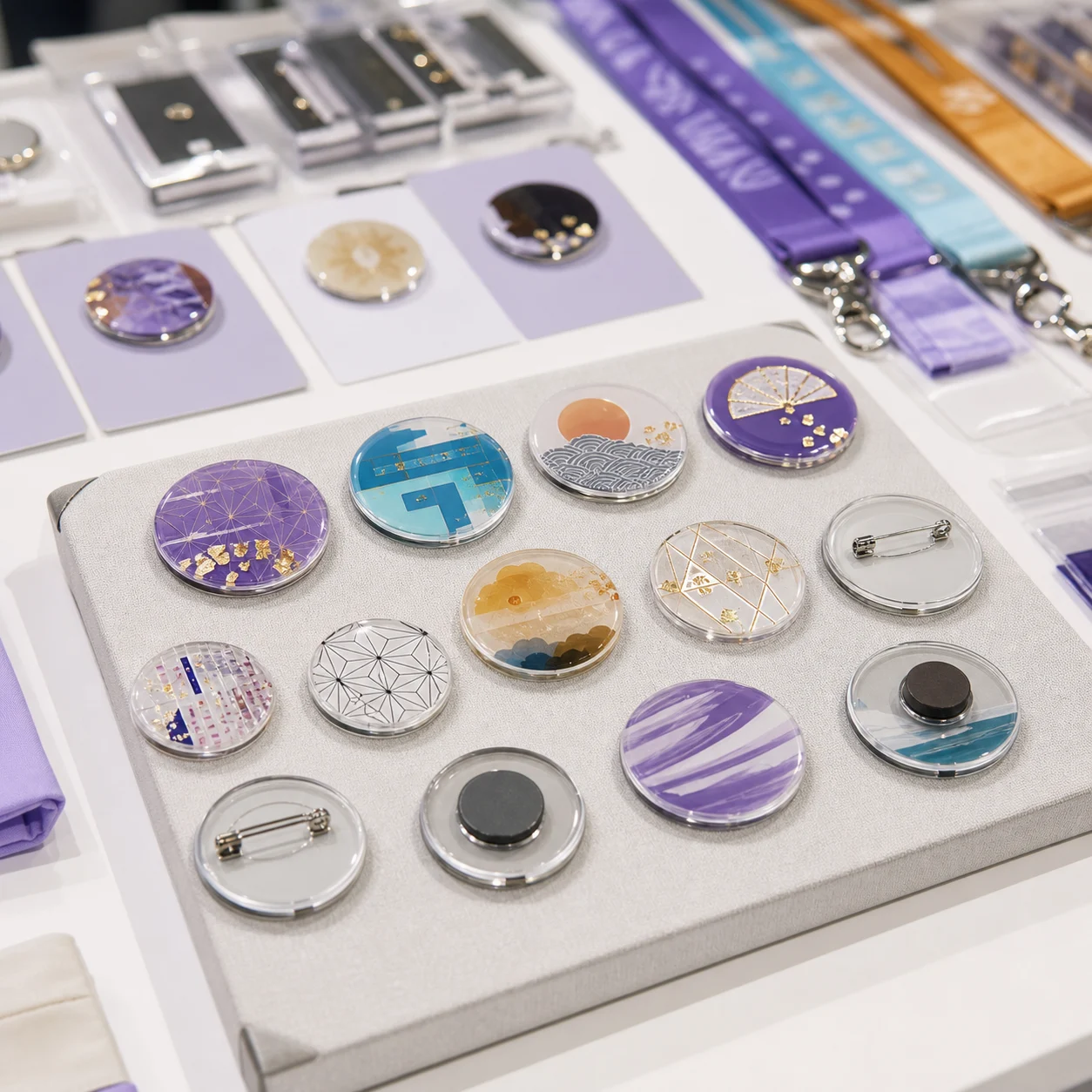 Acrylic badges with pin backs arranged on a tray, printed with gold and violet artwork